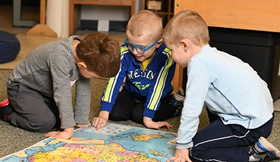 three children pointing at a map on the floor