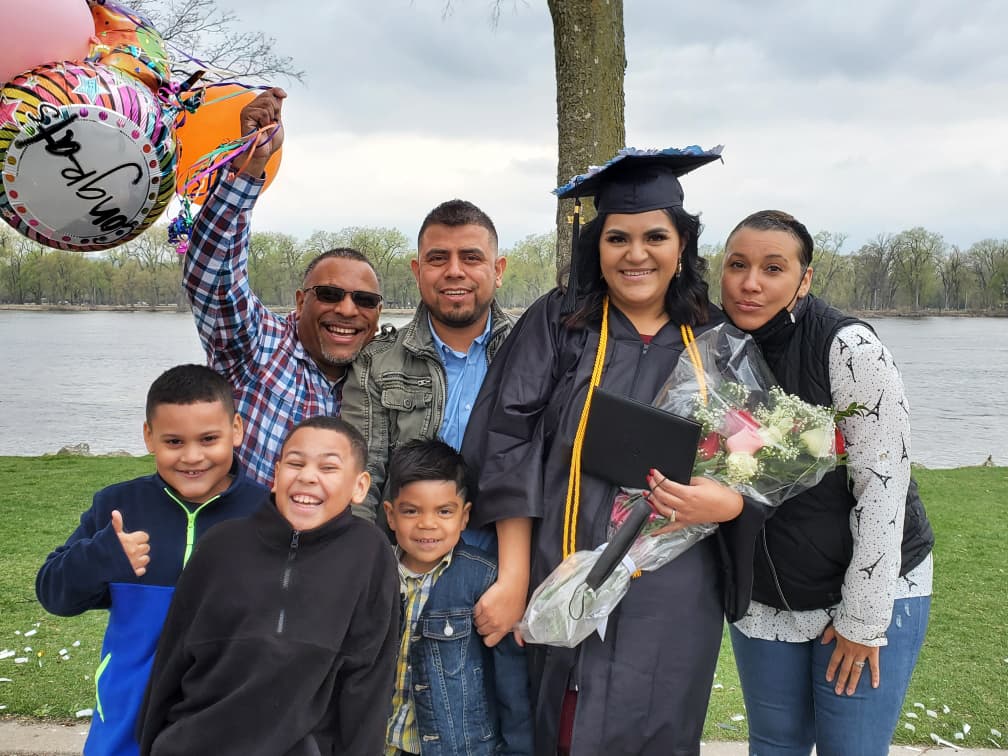 Student dressed in graduation gown poses with family.