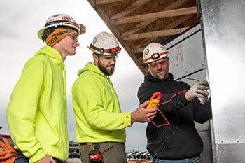 A group of construction workers tests electrical equipment at a jobsite.