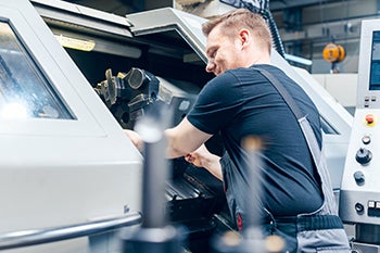 An apprentice works with a larger machine in a workshop.