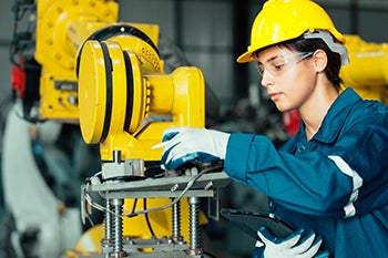 An apprentice in a safety hat works with a large machine at a worksite.
