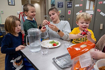 A childhood education apprentice works with three children in a kitchen.