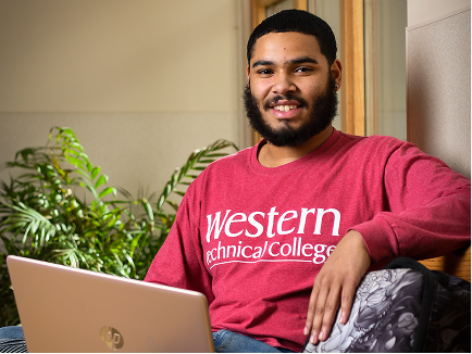 A student in Western gear works on a laptop in a campus lounge.