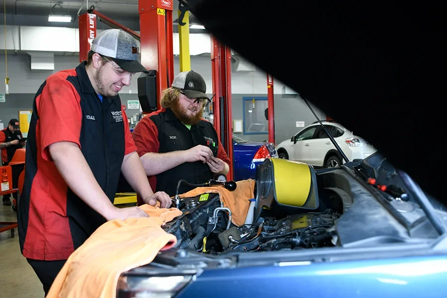 Automotive students work on car engines and interiors in an auto shop.