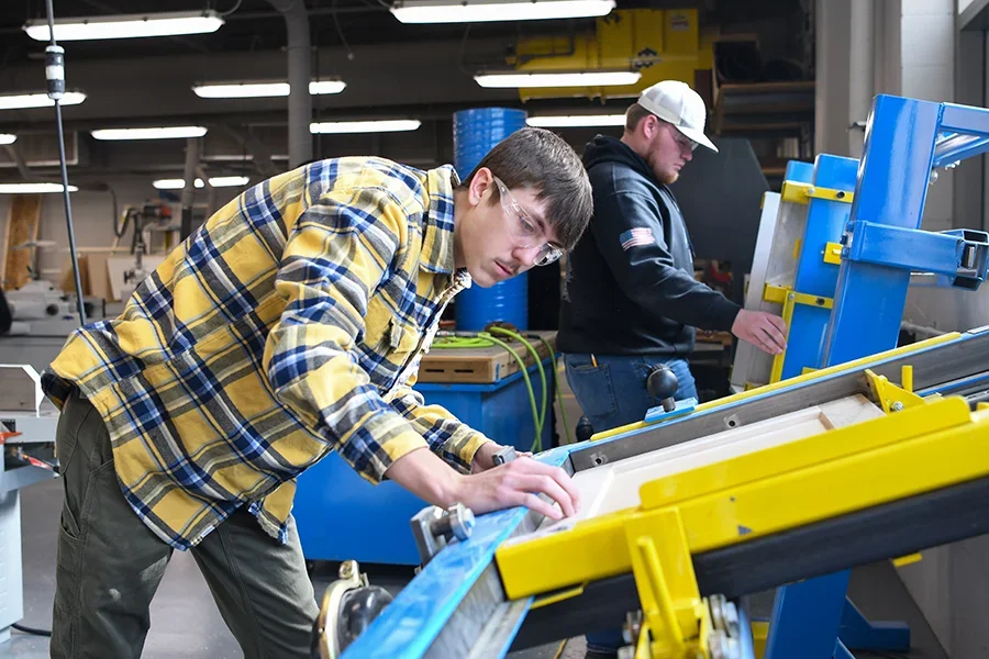 A student works with large machinery to design and build cabinets in a workshop.