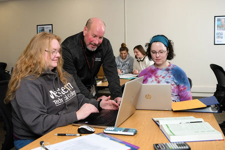 An instructor works with two students in a classroom.