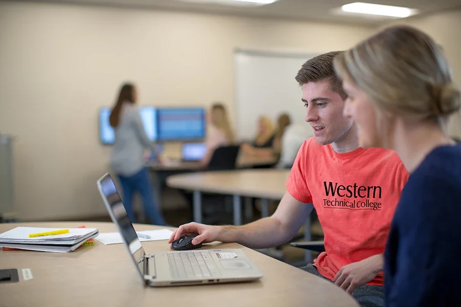 Students collaborate around a laptop in a classroom.