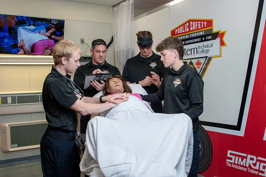 A group of EMT students work together to practice techniques on a dummy in the simulation lab.