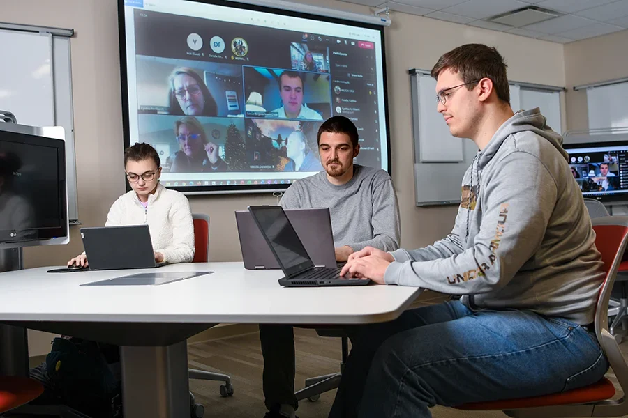 IT students work at laptops around a table during a video call.