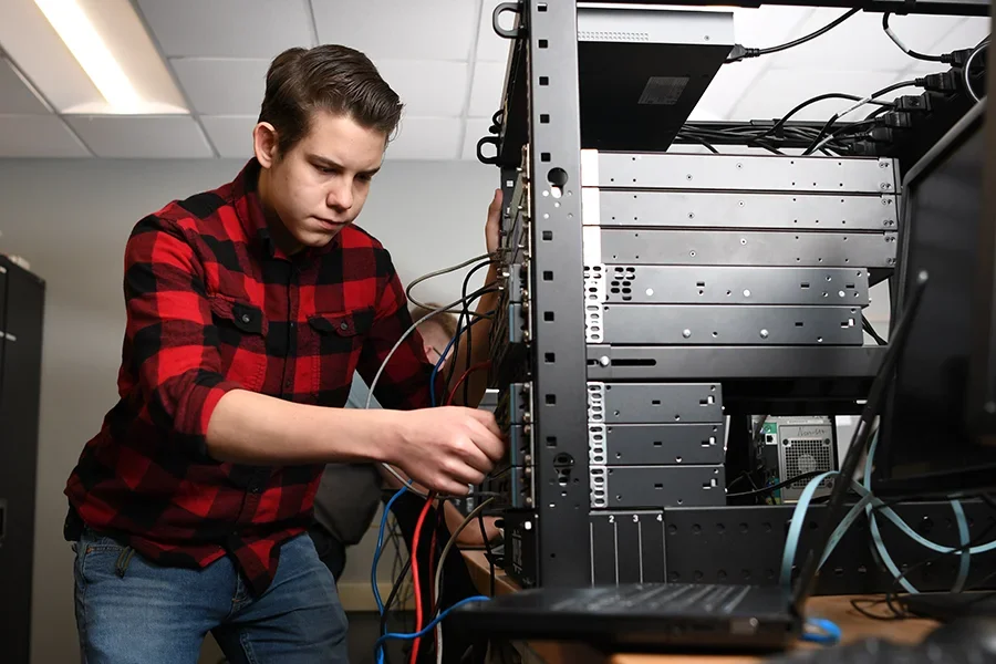 An IT student works wire the wires and equipment in a server room.