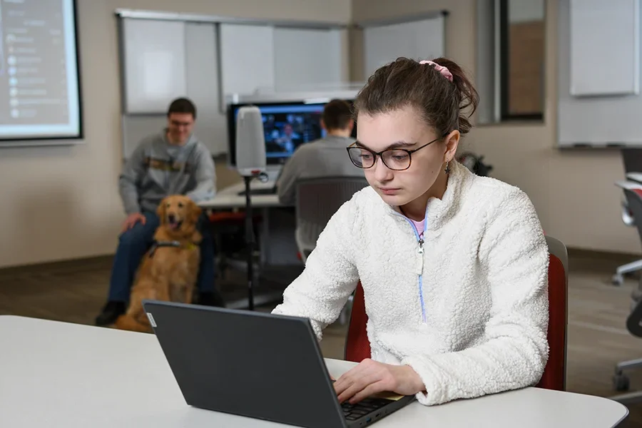 An IT student works at his laptop in a classroom and computer lab.