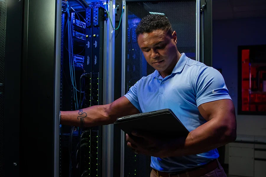 An IT students works with a laptop in a server room.