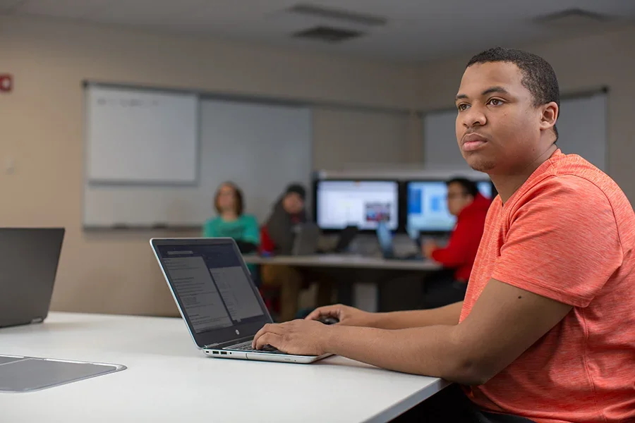 An IT student works on a laptop in a computer lab.