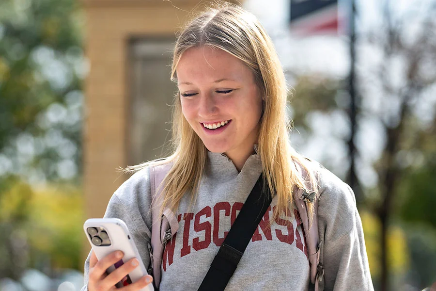 A Western student smiles at her cell phone as she walks on campus