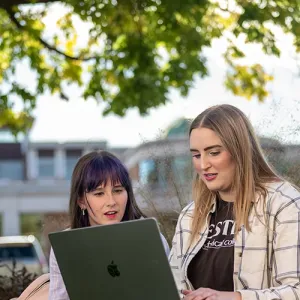 Two female students study outside on Western's campus, with the Student Success Center building in the background