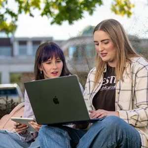 Two female students study outside on Western's campus, with the Student Success Center building in the background