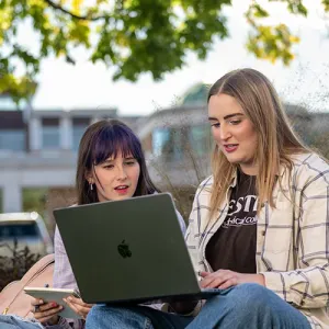 Two female students study outside on Western's campus, with the Student Success Center building in the background