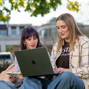 Two female students study outside on Western's campus, with the Student Success Center building in the background