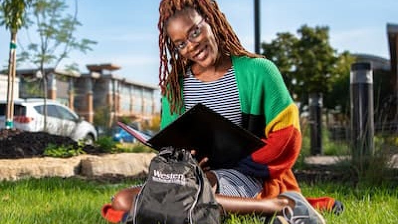 A woman sits in the grass on the Western campus, studying from a binder.