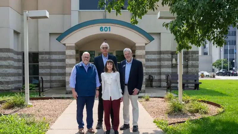 Four people smiling at the camera in front of building.