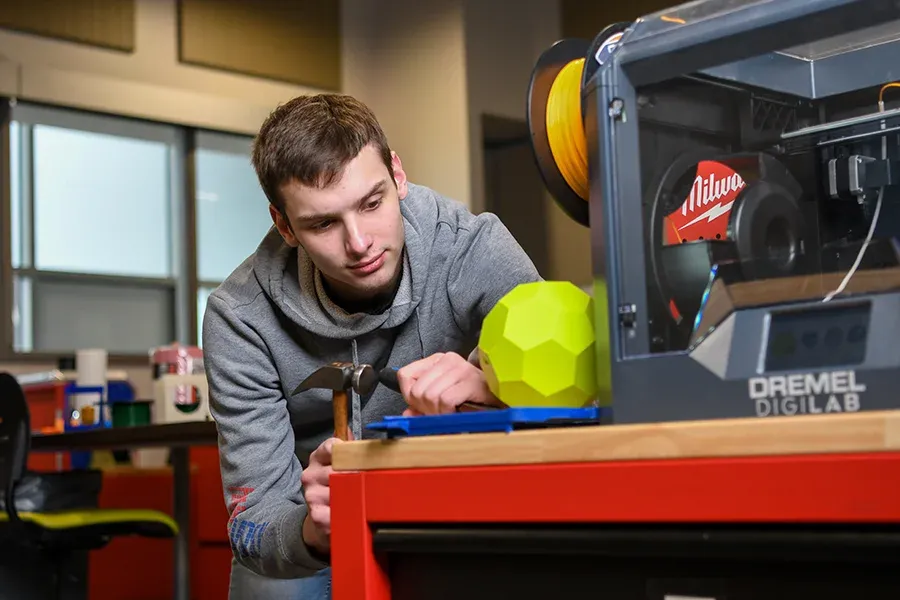 A design student works with a 3D printer in a classroom lab.