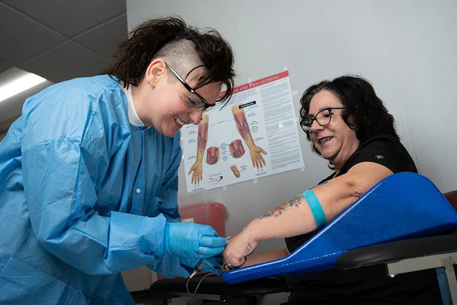 A medical assistant draws blood from a patient in a health office.