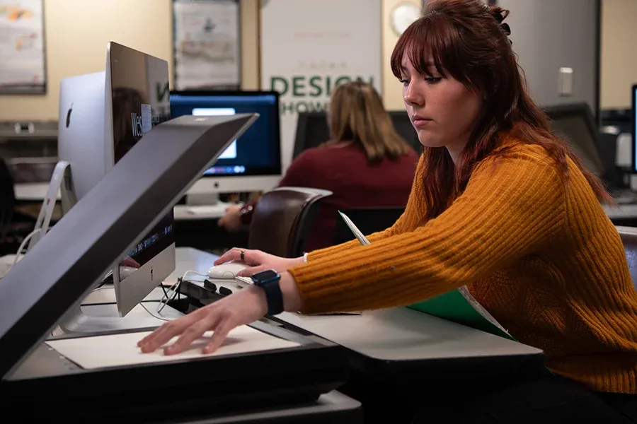 A publishing student works with a tabletop scanner and a computer.