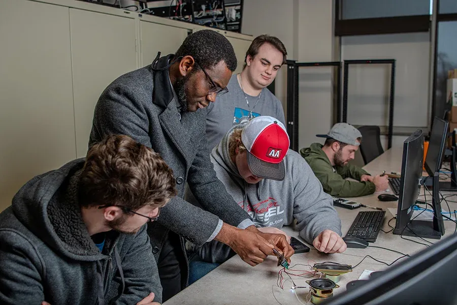 A group of students works together with wires and electronic equipment in a classroom.