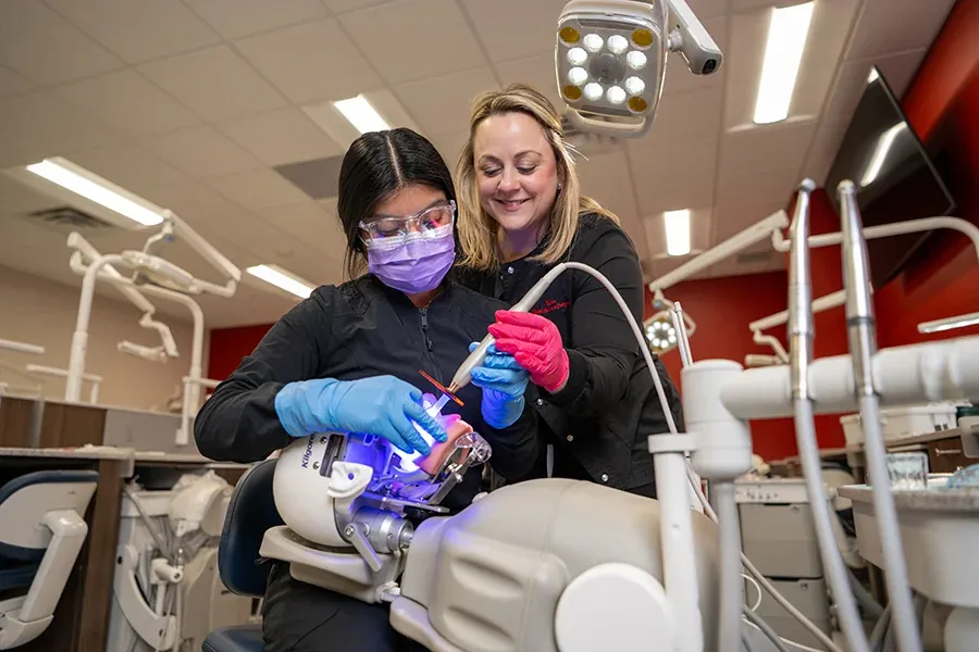 A dental instructor oversees a student practice dental procedures on a dummy.