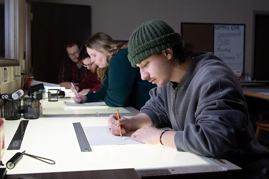 Design students works at drafting boards in a classroom.