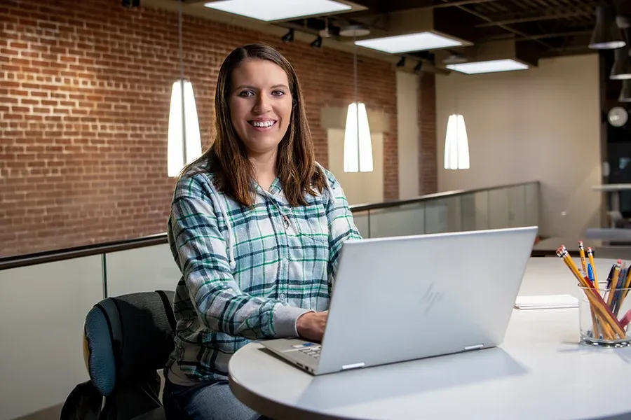 A students sits at her laptop at a table in the library.