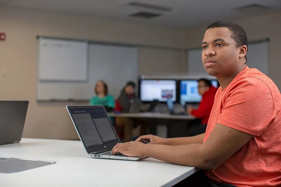An IT student works on a laptop in a computer lab.