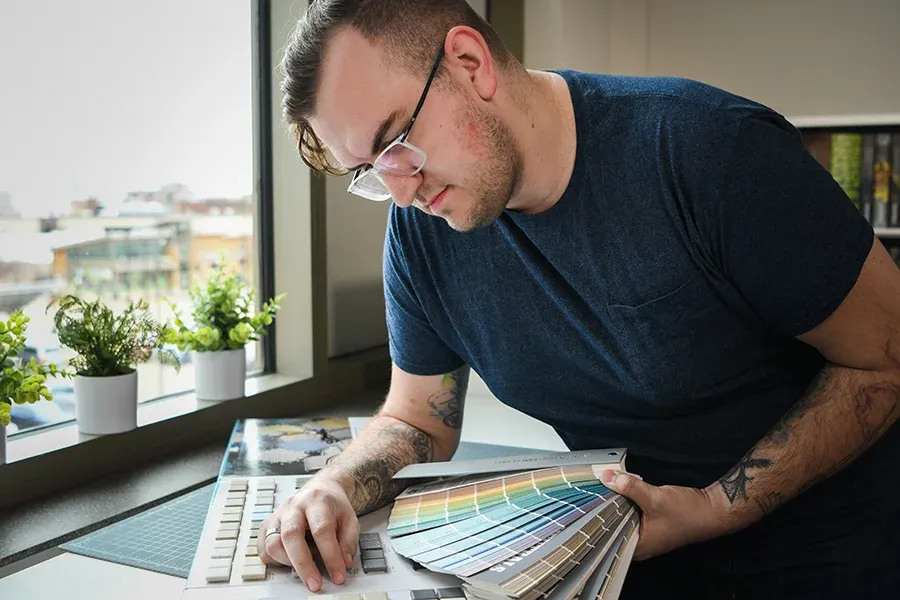 An interior design students looks over paint-color palettes and design materials at a desk.
