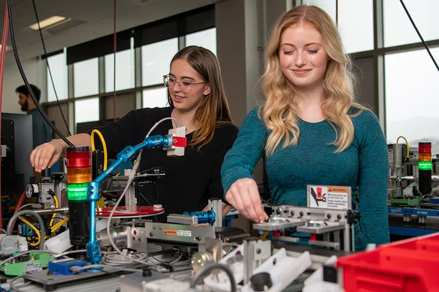Two technology students work with wires and electrical components in a lab.
