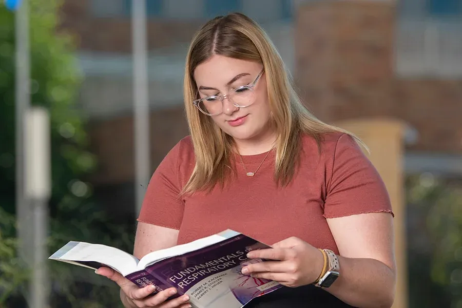 A female student reading a textbook outside in the Cleary Courtyard