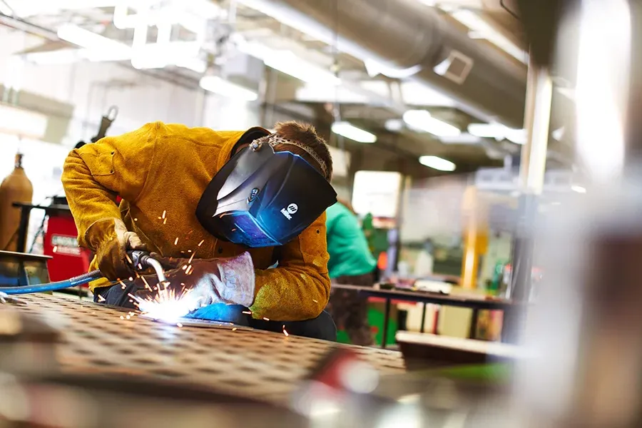 A welding student uses a torch in a workshop.
