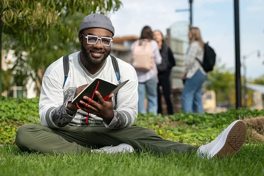 A male student sits outside at Western while other students talk behind him