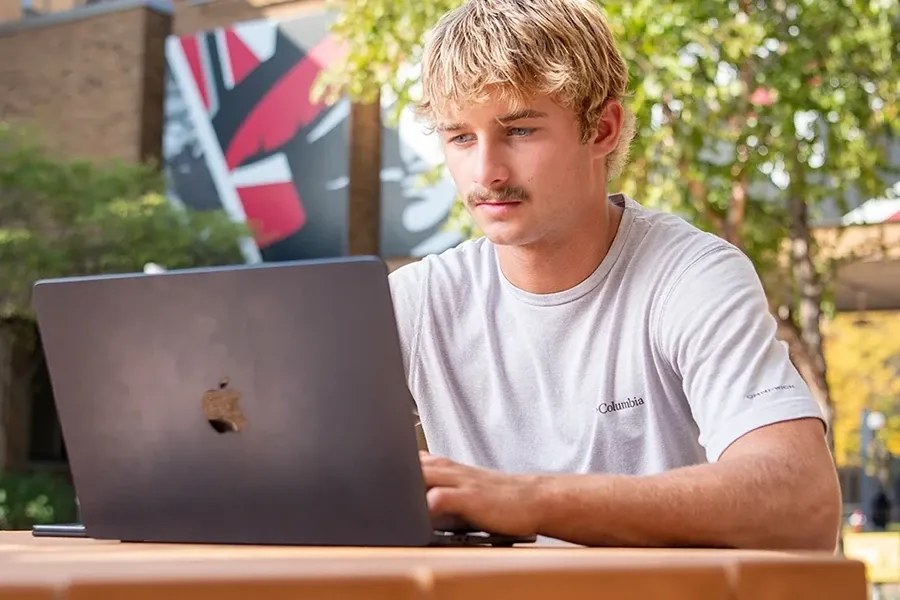 A student with a laptop studies outside in the Cleary Courtyard
