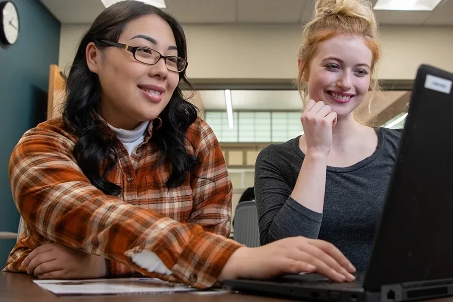 Two students work together on a laptop in a classroom