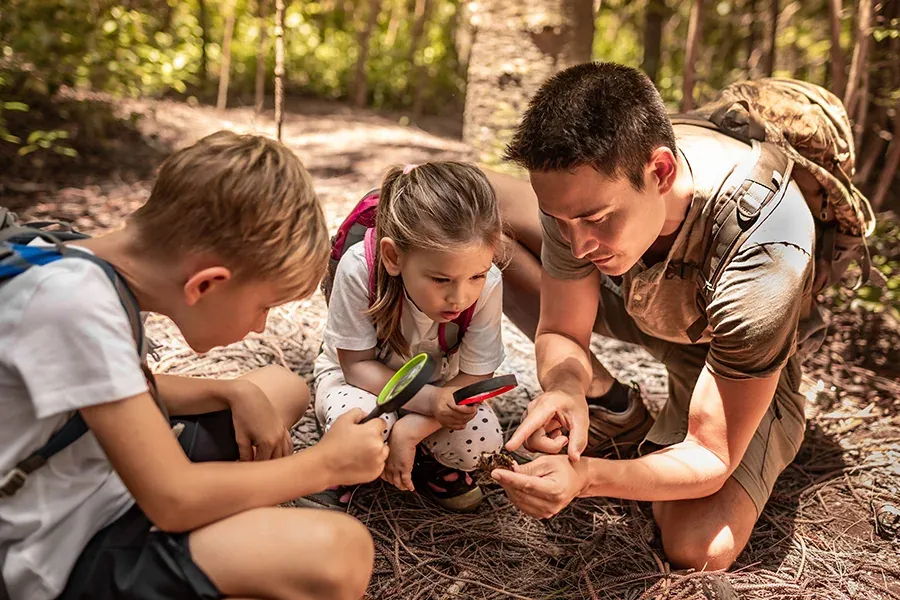 A male teacher and two young students examine a leaf along a trail