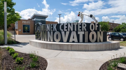 Entrance of Wanek Center of Innovation with metallic signage and robotic arm sculpture in front of a modern building.