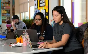 Students work on laptops in a common space.