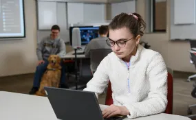 An IT student works at his laptop in a classroom and computer lab.