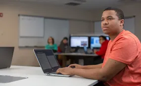 An IT student works on a laptop in a computer lab.